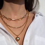 Arany nyakláncokat visel egy barna hajú nő fehér ingben